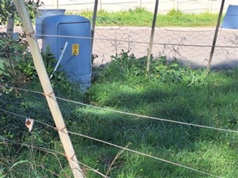 A view of the property boundary featuring wire mesh fencing and an electrical utility box located near the street.