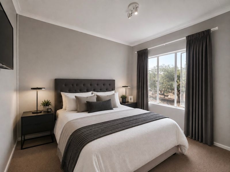 A well-maintained bedroom featuring neutral wall tones, carpeted flooring, and a large window providing natural light and garden views.