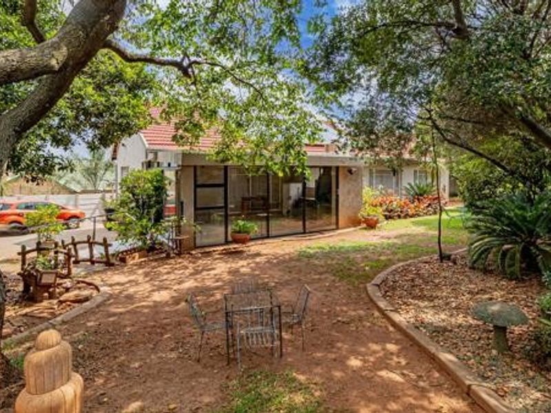 Rear view of the property featuring a landscaped garden, mature trees, and an enclosed patio area with aluminum framing.