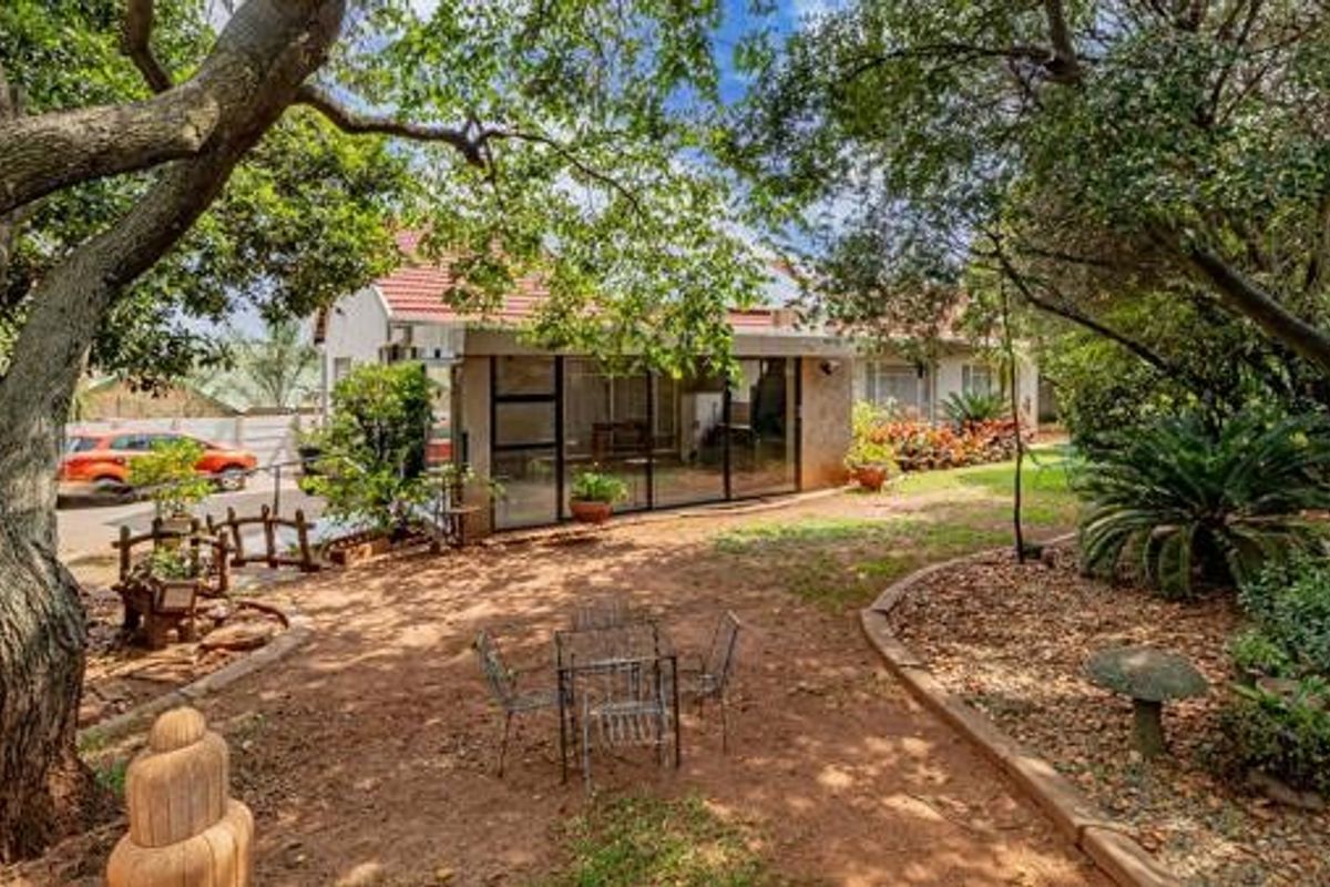 Rear view of the property featuring a landscaped garden, mature trees, and an enclosed patio area with aluminum framing.