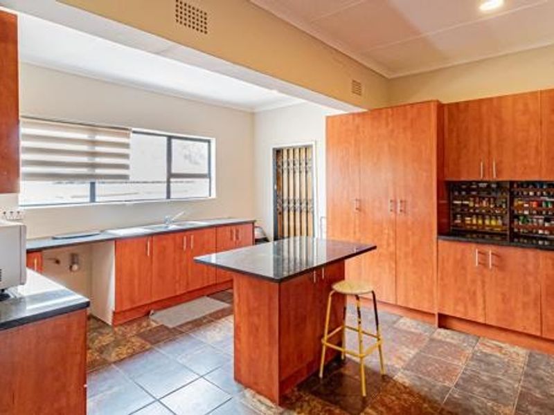 Spacious kitchen featuring extensive wood-finish cabinetry, a central island with breakfast seating, dark stone countertops, and durable tiled flooring.
