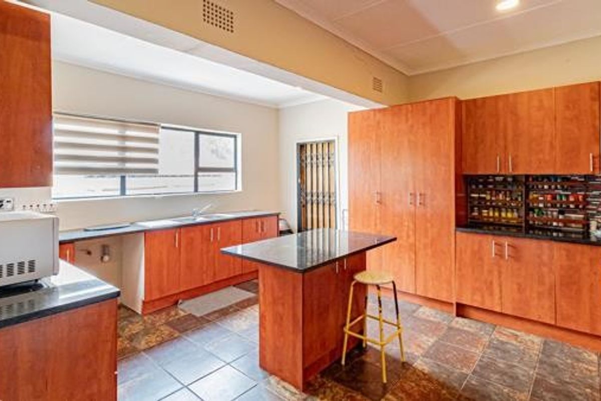 Spacious kitchen featuring extensive wood-finish cabinetry, a central island with breakfast seating, dark stone countertops, and durable tiled flooring.