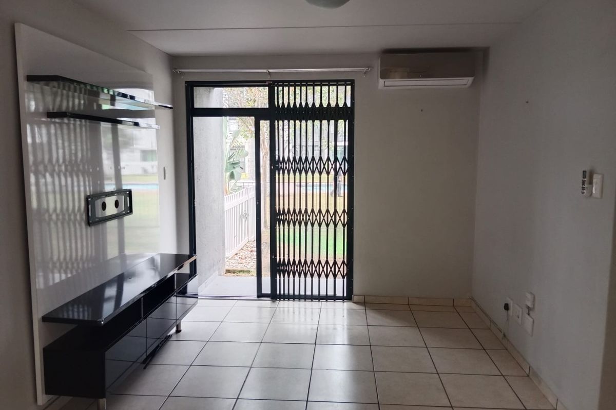An empty living room featuring tiled flooring, a built-in media console, a split-system air conditioner, and a sliding door with a security gate.