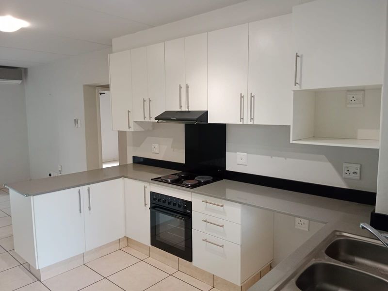 Modern kitchen featuring white cabinetry, stone countertops, built-in electric oven and stove, and tiled flooring in a clean, open-plan layout.