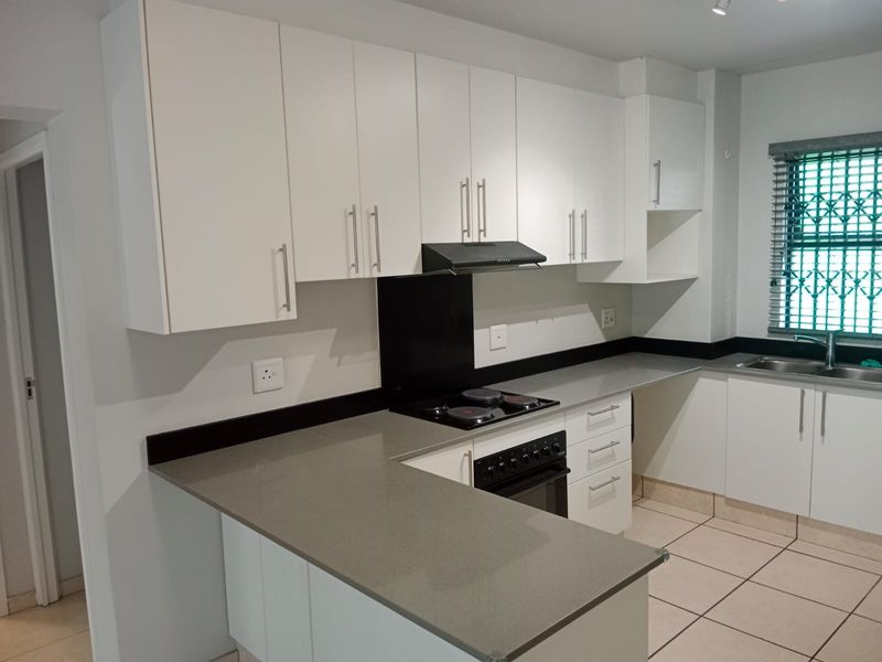 Modern kitchen featuring white cabinetry, stone countertops, built-in oven, electric hob, extractor fan, and tiled flooring.