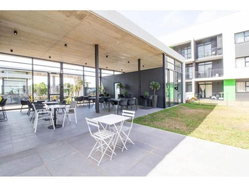 A modern covered patio area featuring a concrete ceiling, tiled flooring, and extensive glass walls, providing a seamless transition to the outdoor garden space.