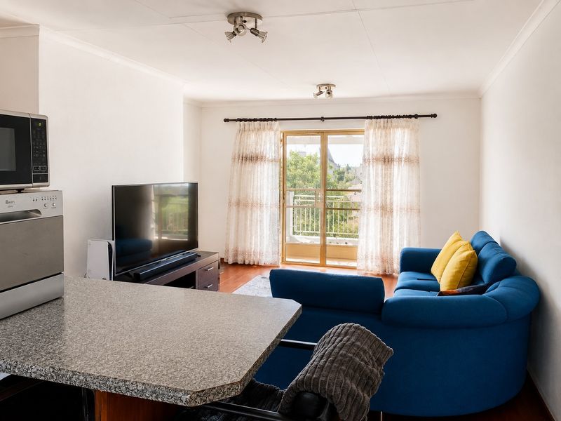 Open plan living area featuring laminate flooring, a breakfast counter, and sliding glass doors leading to a private balcony.