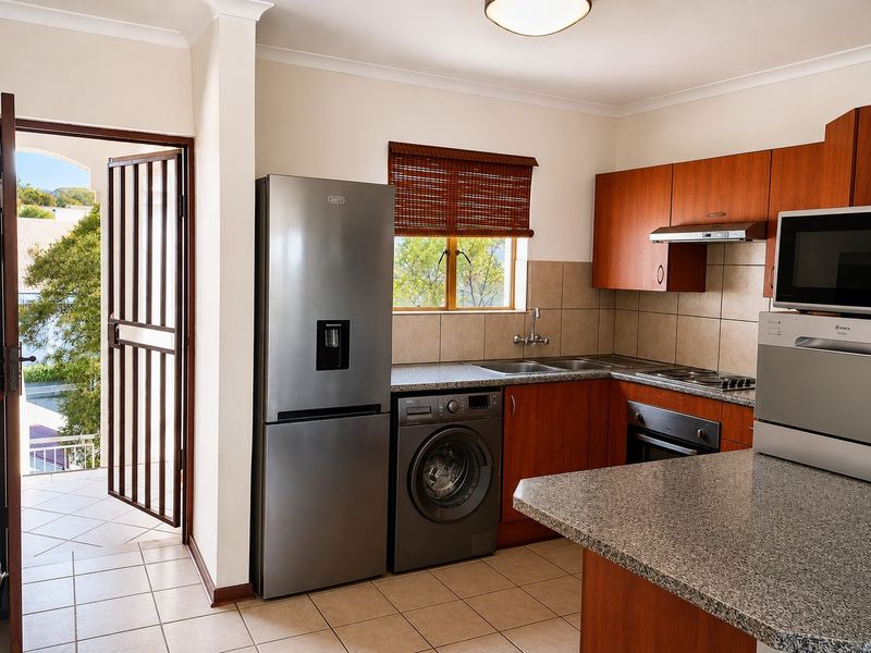 Functional kitchen featuring granite countertops, wooden cabinetry, built-in oven, extractor fan, and tiled flooring, with direct access to an outdoor balcony area.