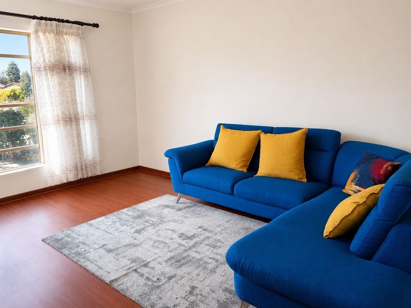 A bright living room featuring laminate flooring, coving, and a large window providing natural light and outdoor views.