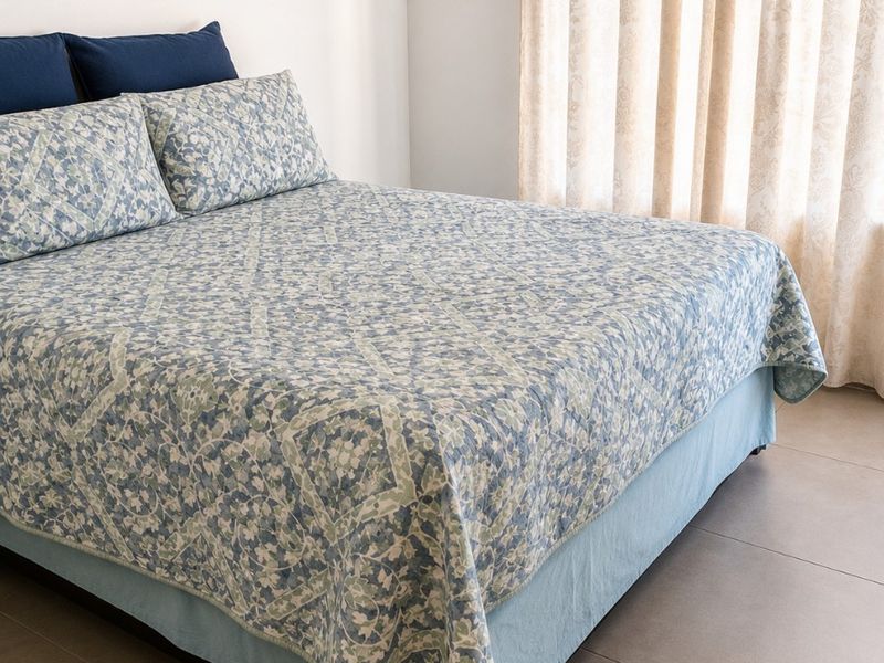A bedroom featuring neutral tiled flooring and natural light provided by a window with curtains.