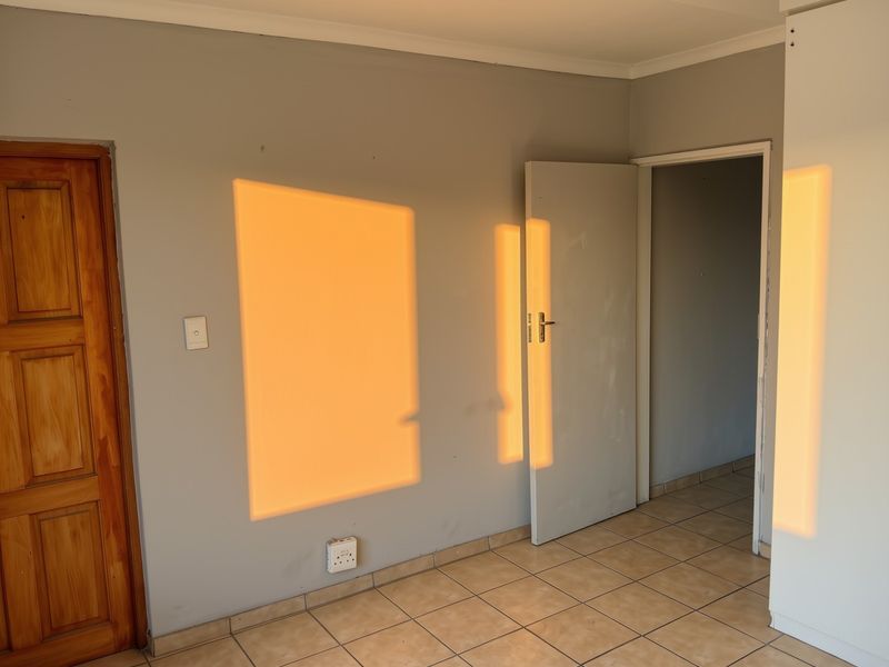 An empty bedroom featuring tiled flooring, neutral wall finishes, and two internal doors, illuminated by natural sunlight.