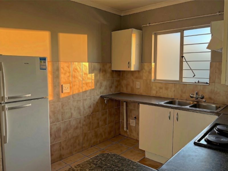 A functional kitchen featuring laminate countertops, double stainless steel sink, built-in cabinetry, and tiled splashbacks, offering a practical layout for daily use.