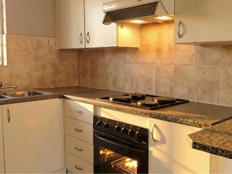 A functional kitchen featuring built-in cabinetry, laminate countertops, a double sink, and integrated cooking appliances including an oven, hob, and extractor fan.