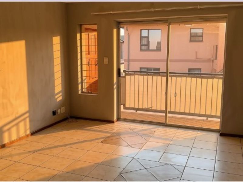 An empty living room featuring tiled flooring and a sliding glass door leading to a balcony with security bars.