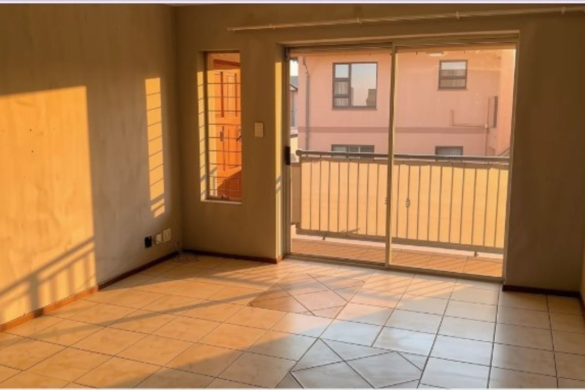 An empty living room featuring tiled flooring and a sliding glass door leading to a balcony with security bars.