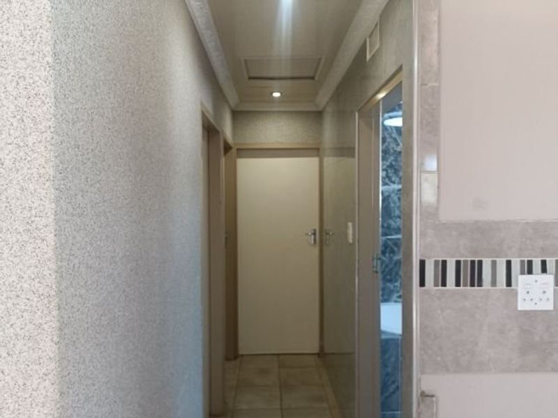 A clean and functional hallway featuring tiled flooring, recessed ceiling lighting, and decorative cornice detailing, providing access to adjacent rooms.
