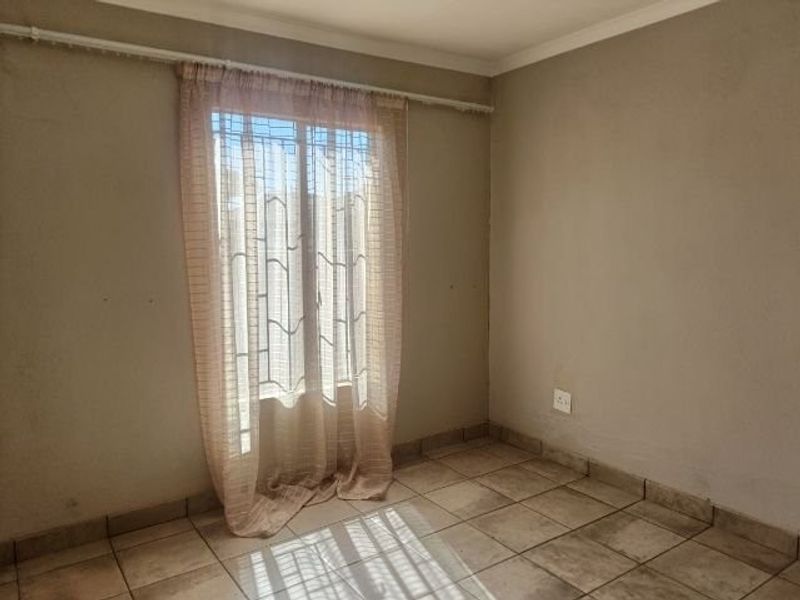 An empty bedroom featuring tiled flooring, a window with security bars, and neutral wall tones, offering a blank canvas for personalization.