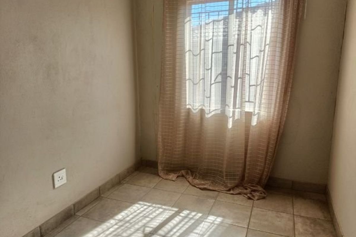 A compact, empty bedroom featuring ceramic floor tiles, a window with security bars, and neutral wall finishes.