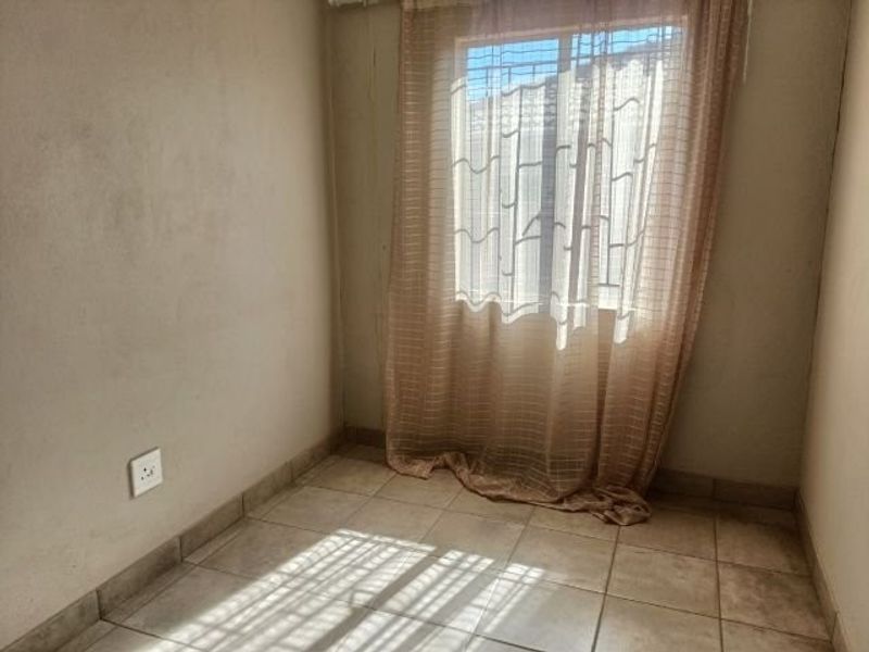 A compact, empty bedroom featuring ceramic floor tiles, a window with security bars, and neutral wall finishes.