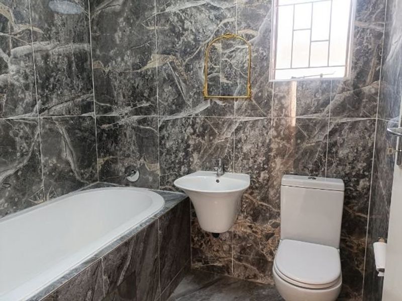 A modern bathroom featuring marble-effect wall tiling, a built-in bathtub, a wall-mounted basin, and a toilet.