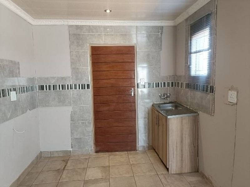 A partially finished kitchen area featuring tiled flooring, a single basin sink, and tiled splashbacks, requiring completion of wall finishes and fixtures.