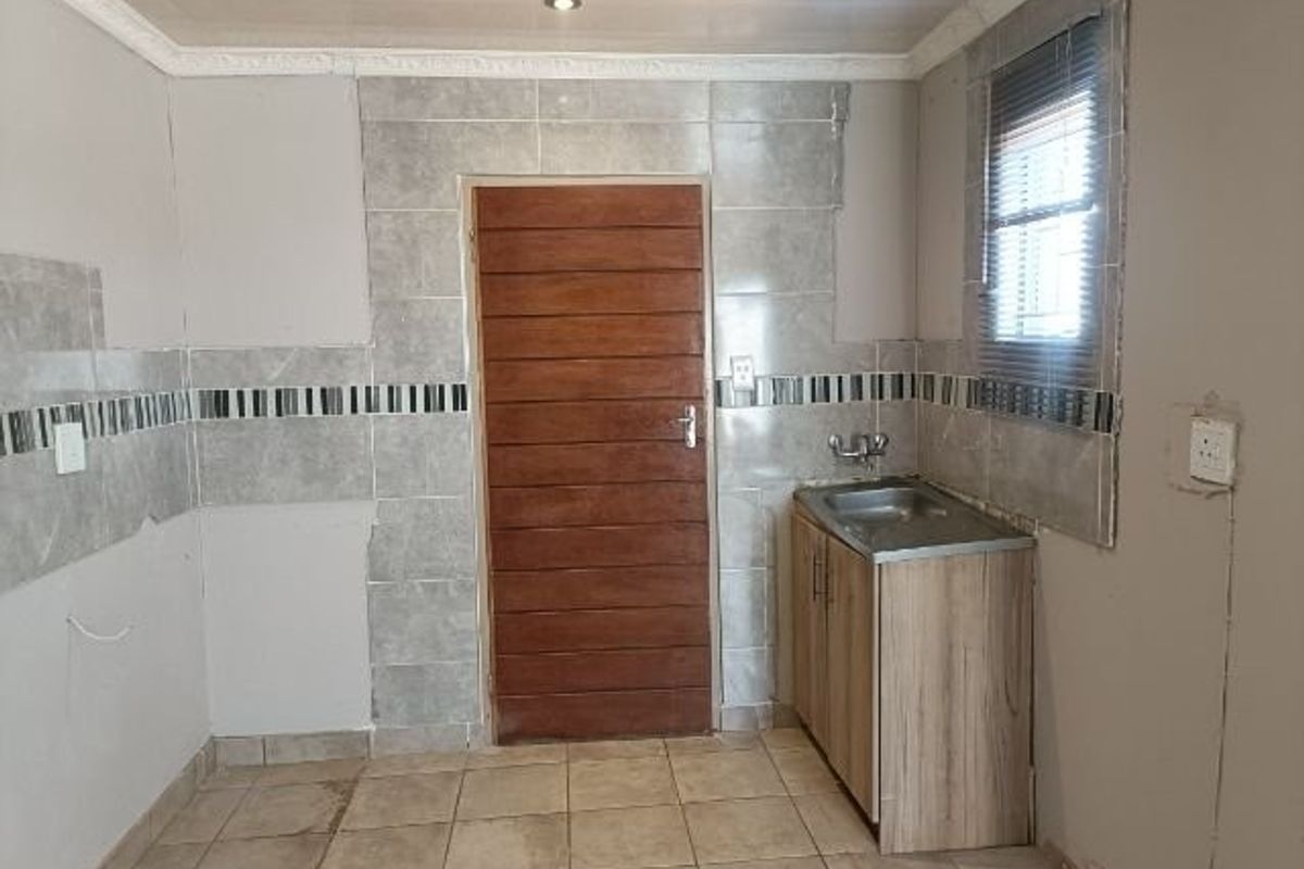 A partially finished kitchen area featuring tiled flooring, a single basin sink, and tiled splashbacks, requiring completion of wall finishes and fixtures.