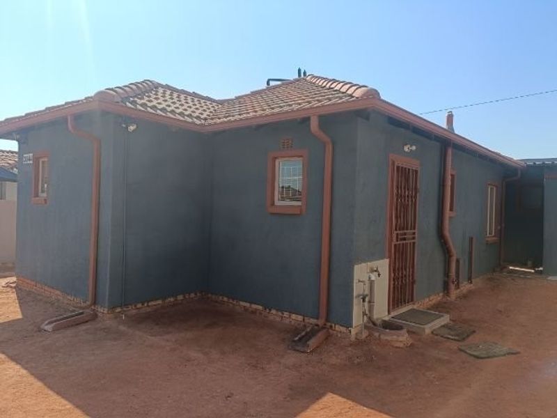Rear exterior view of the house featuring a tiled roof, dark rendered walls, security gate, and functional rainwater drainage system.