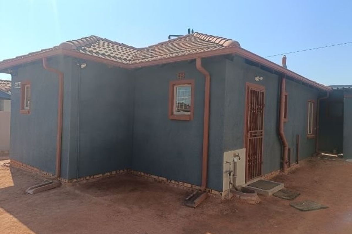 Rear exterior view of the house featuring a tiled roof, dark rendered walls, security gate, and functional rainwater drainage system.