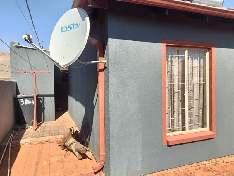 Rear exterior view of the house featuring a satellite dish, security bars on the window, and a paved walkway.