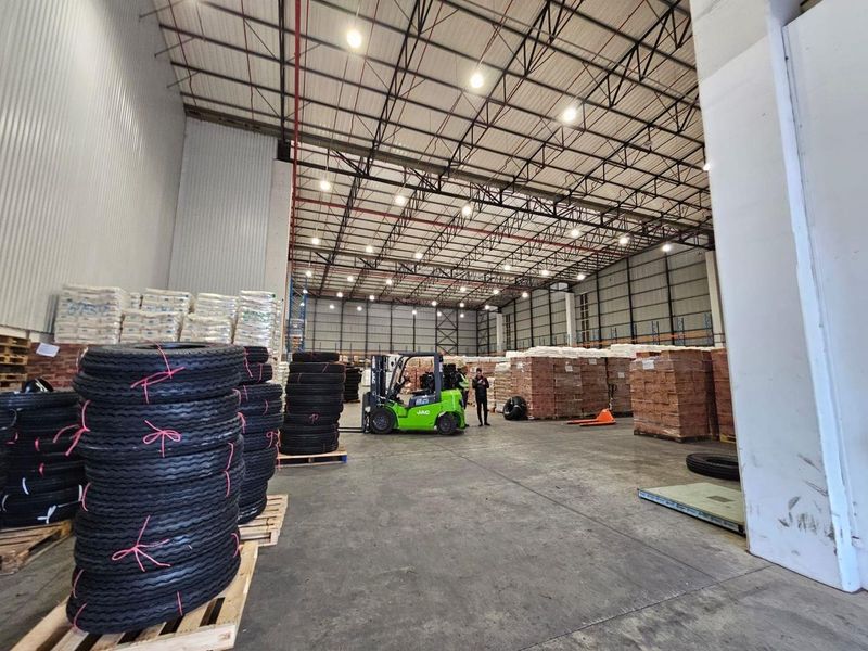 Spacious industrial warehouse featuring high ceilings with exposed steel trusses, high bay lighting, concrete flooring, and metal wall cladding, suitable for storage or logistics.