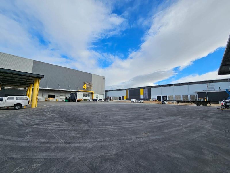 Spacious industrial warehouse exterior featuring a large concrete yard, multiple loading bays, and modern steel cladding with clear signage.