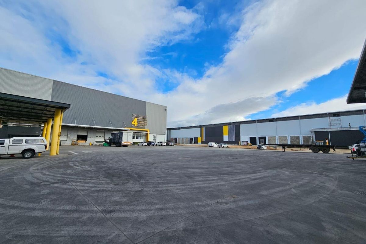 Spacious industrial warehouse exterior featuring a large concrete yard, multiple loading bays, and modern steel cladding with clear signage.