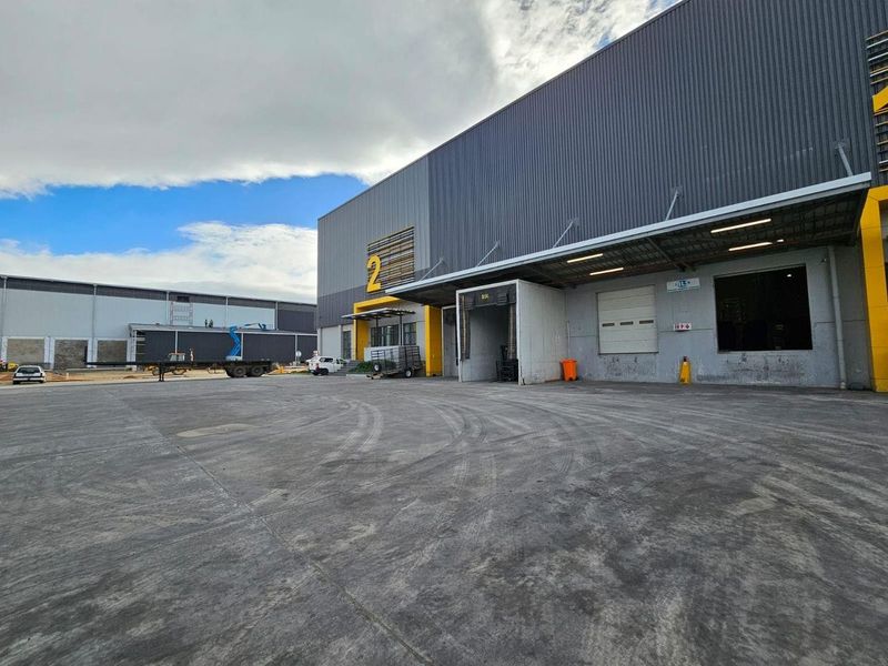 Industrial warehouse exterior featuring a large concrete yard, loading dock access, and modern metal cladding facade.