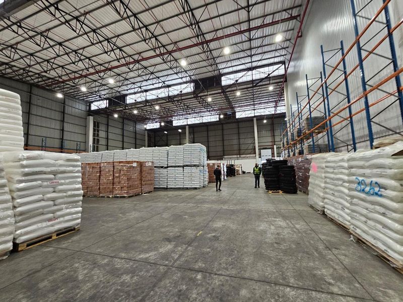 Spacious industrial warehouse featuring high ceilings with exposed steel trusses, high bay lighting, concrete flooring, and integrated metal racking systems.