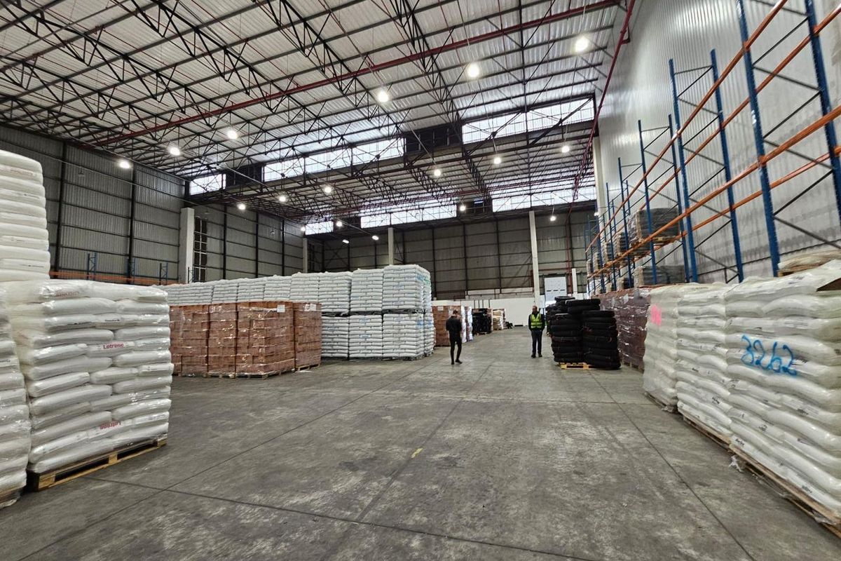 Spacious industrial warehouse featuring high ceilings with exposed steel trusses, high bay lighting, concrete flooring, and integrated metal racking systems.