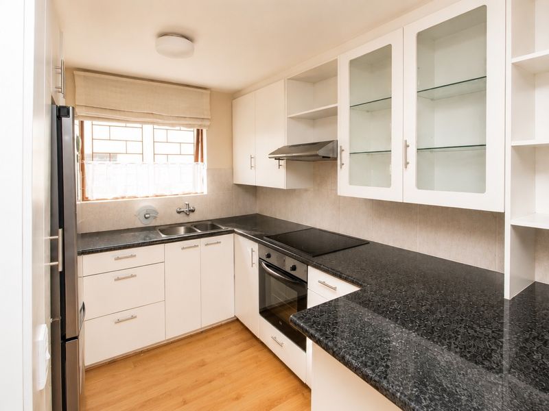 A well-maintained kitchen featuring white cabinetry, dark granite countertops, integrated oven and hob, and ample storage space with glass-fronted display units.