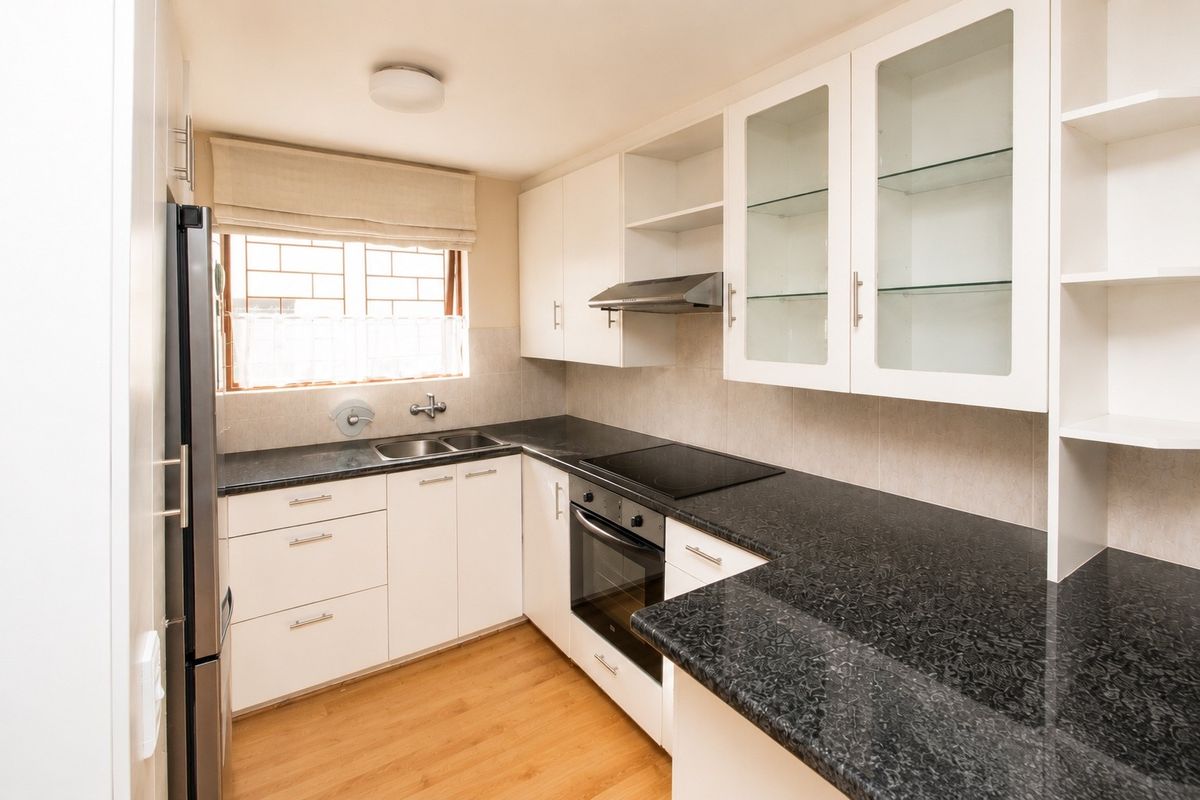A well-maintained kitchen featuring white cabinetry, dark granite countertops, integrated oven and hob, and ample storage space with glass-fronted display units.