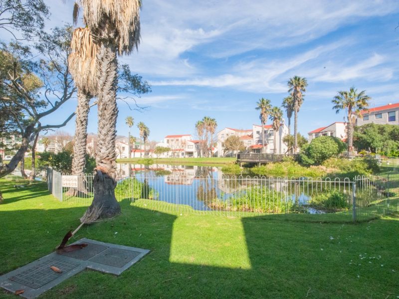 A scenic view of a communal pond and landscaped garden area surrounded by residential apartment buildings and mature palm trees.