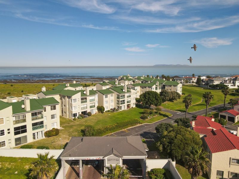 Aerial view of the Greenways estate, showcasing the secure gated entrance, multi-story apartment blocks with green roofs, and proximity to the coastline.