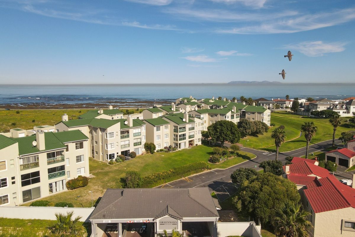 Aerial view of the Greenways estate, showcasing the secure gated entrance, multi-story apartment blocks with green roofs, and proximity to the coastline.