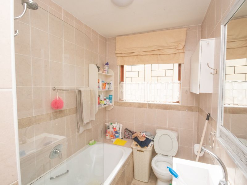 A functional bathroom featuring a bathtub with an integrated shower, wall-mounted basin, toilet, and neutral wall tiling.