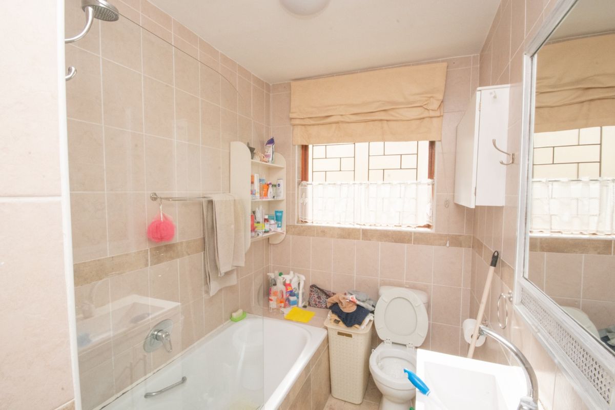 A functional bathroom featuring a bathtub with an integrated shower, wall-mounted basin, toilet, and neutral wall tiling.