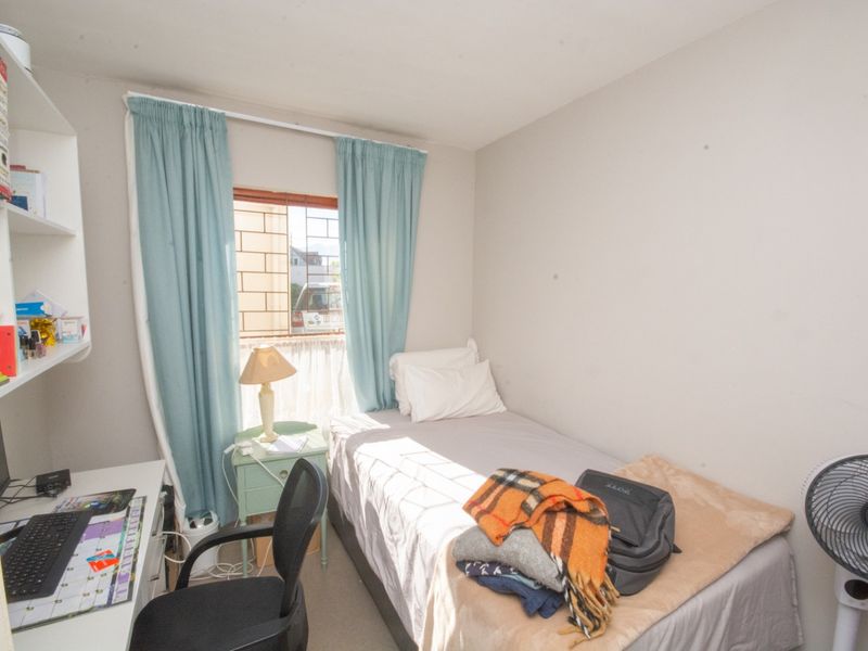 A compact bedroom featuring built-in shelving and a window with security bars, providing a functional space for rest or study.