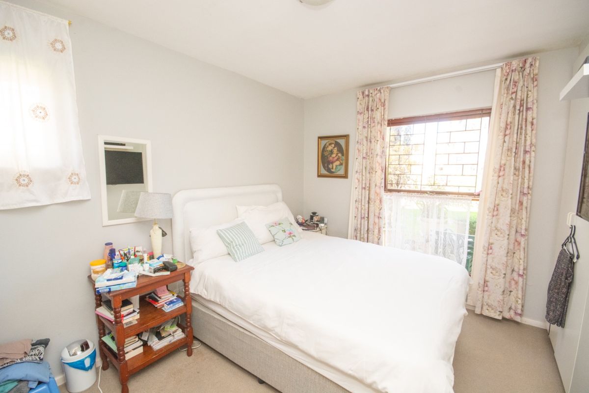 A functional bedroom featuring carpeted flooring and a window fitted with security bars, providing natural light and a standard layout.