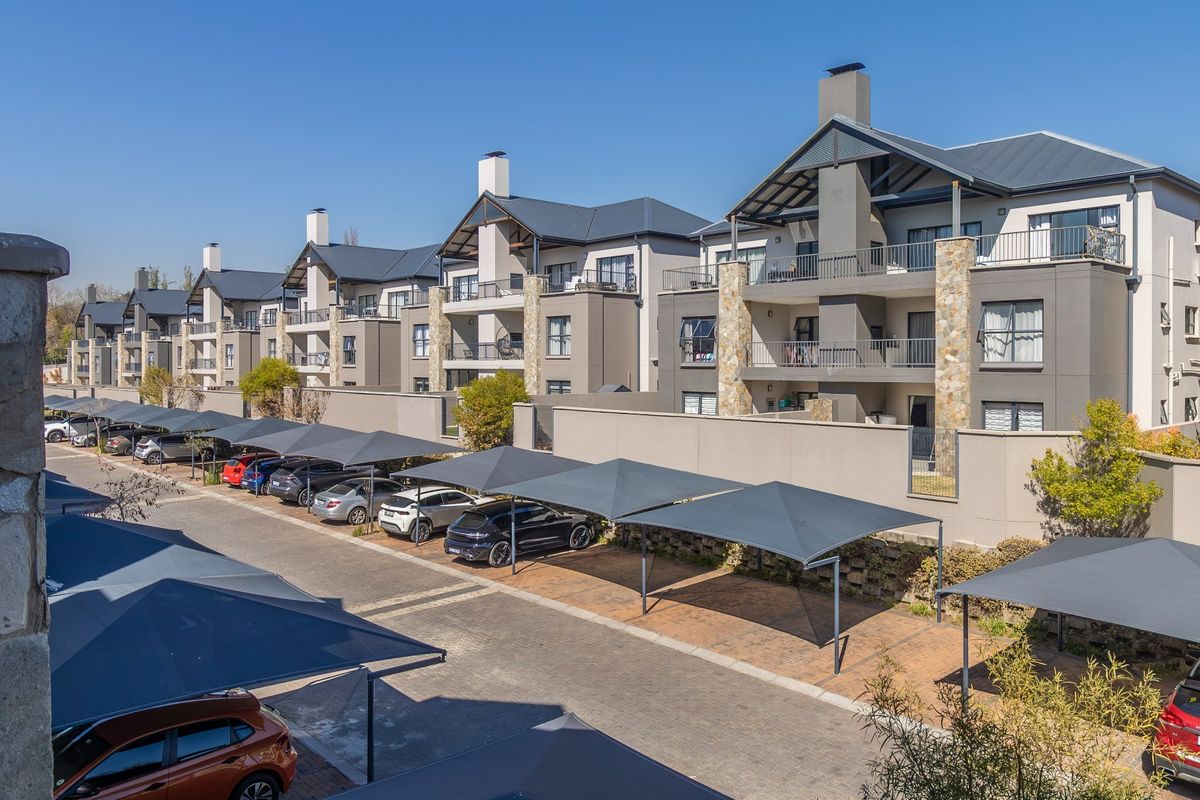 Exterior view of a modern apartment complex featuring multiple levels, private balconies, stone-clad accents, and covered parking bays for residents.