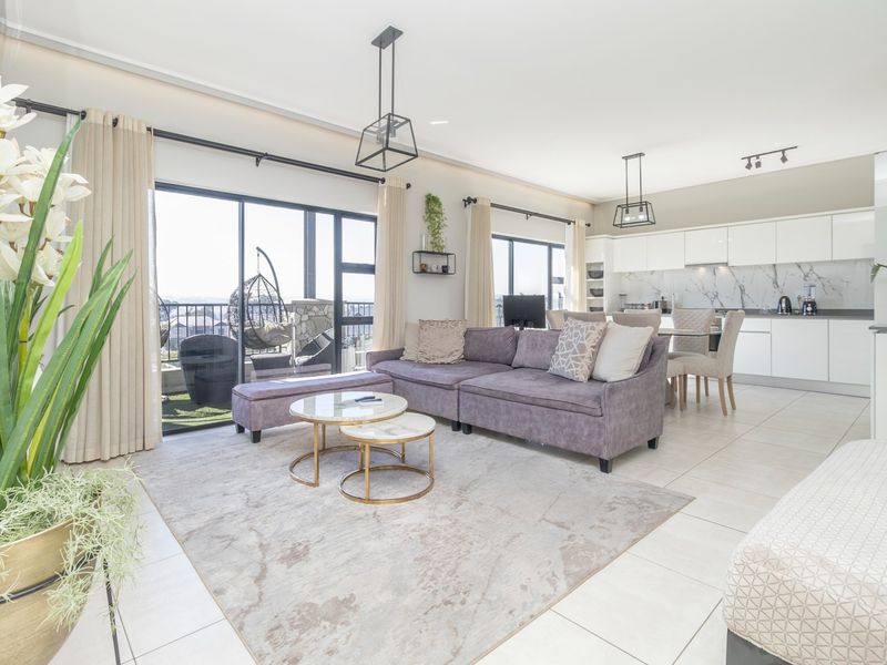 Modern open-plan living area featuring a sleek kitchen with marble-look backsplash, tiled floors, and large sliding doors leading to a balcony.