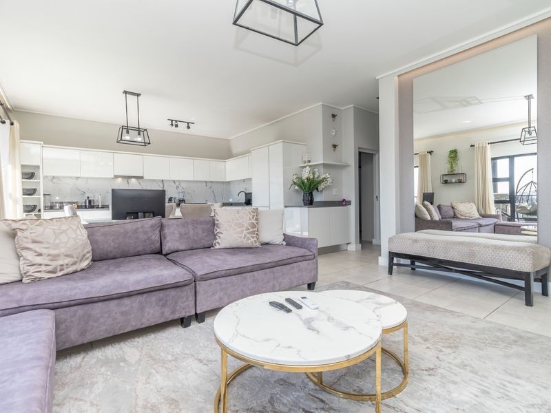 Modern open-plan living area featuring a sleek kitchen with marble-look backsplash, tiled floors, and a spacious layout connecting to the lounge.