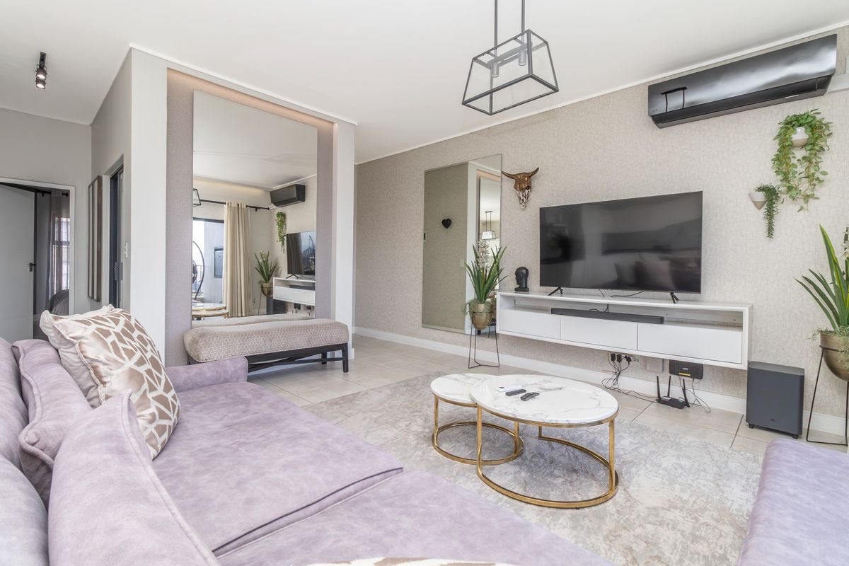 A well-maintained living room featuring tiled flooring, textured wallpaper, a wall-mounted air conditioning unit, and modern recessed and pendant lighting.