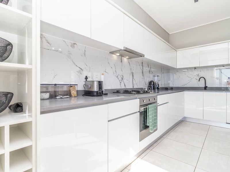 A modern, well-maintained kitchen featuring sleek white cabinetry, marble-look splashbacks, stone countertops, and high-quality built-in appliances.