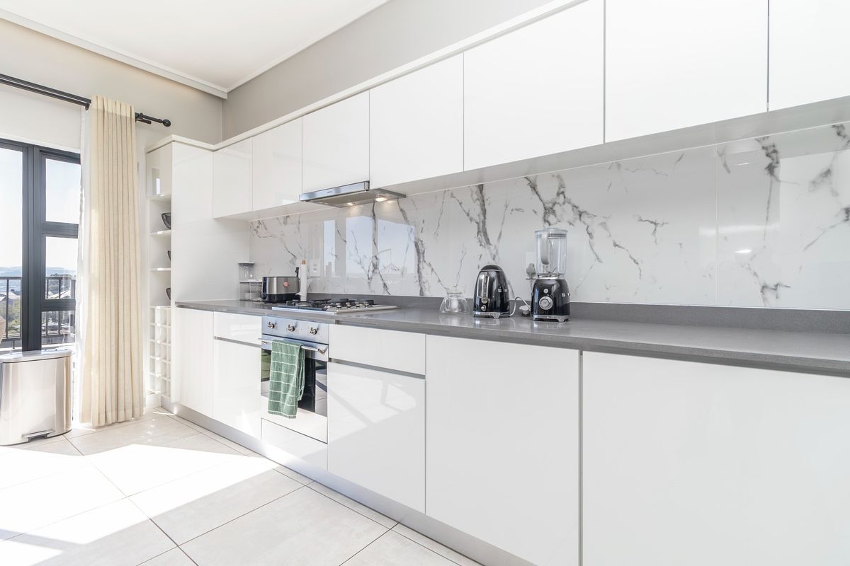 Modern kitchen featuring white gloss cabinetry, marble-look splashback, stone countertops, and integrated appliances, with direct access to a balcony.